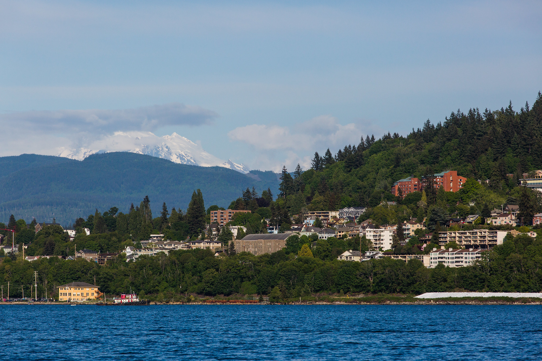 View of Bellingham and Western Washington University from the bay with Mount Baker behind some clouds in the distance 